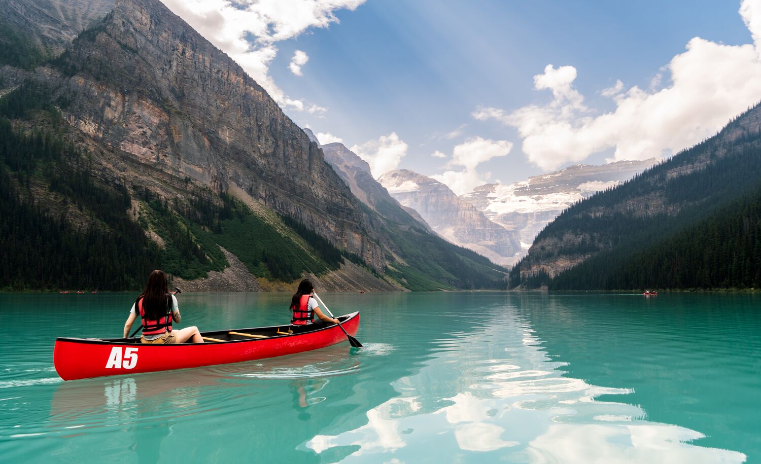 Two friends paddle in a canoe in an open lake surrounded by mountains in Lake Louise.